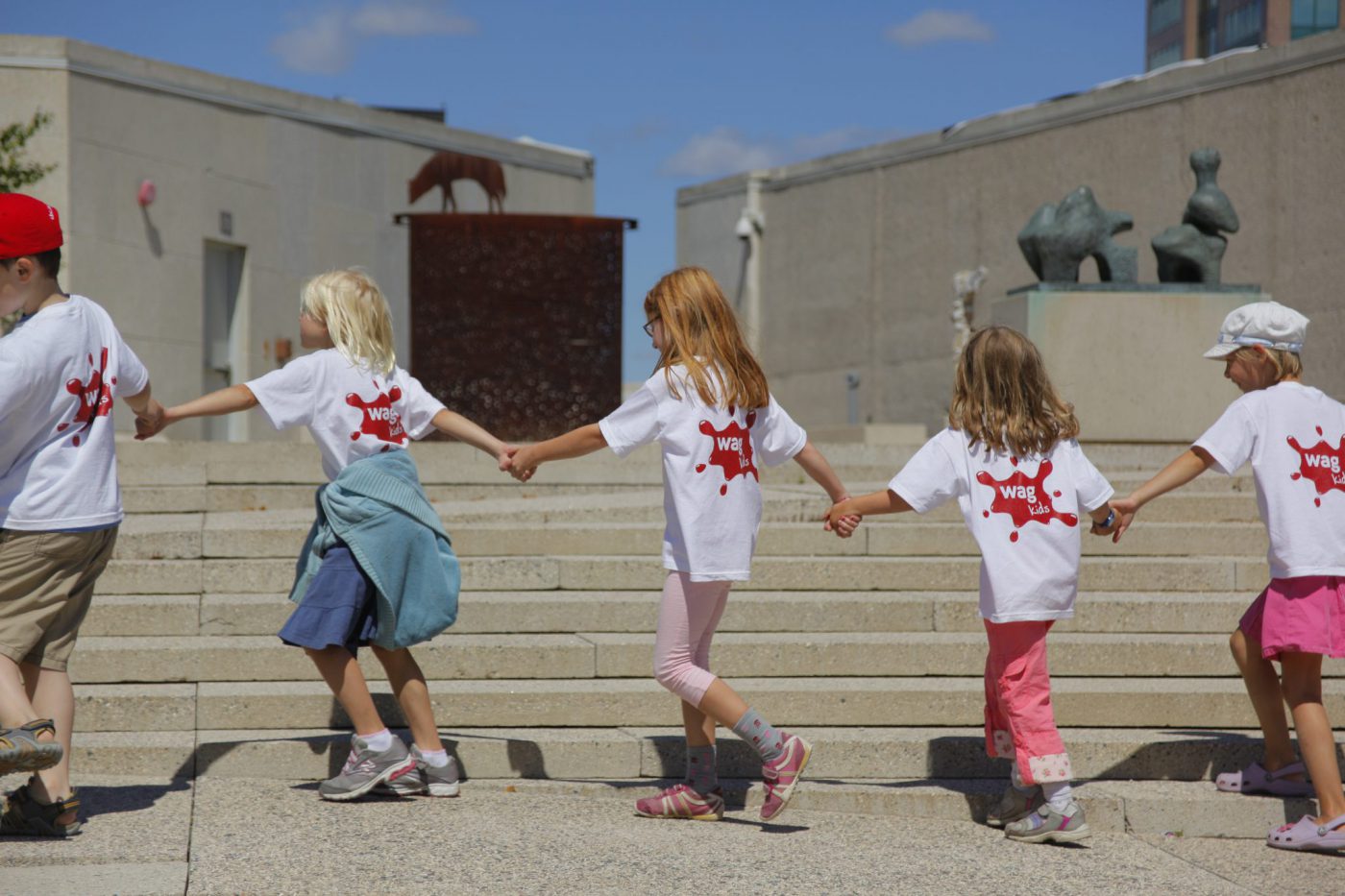 Kids at a WAG Art Camp holding hands while walking in a line.