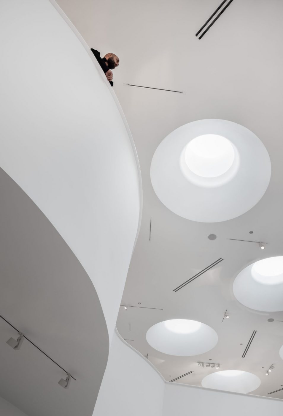 A person looks over the edge of a white balcony in a Winnipeg Art Gallery-Qaumajuq gallery.