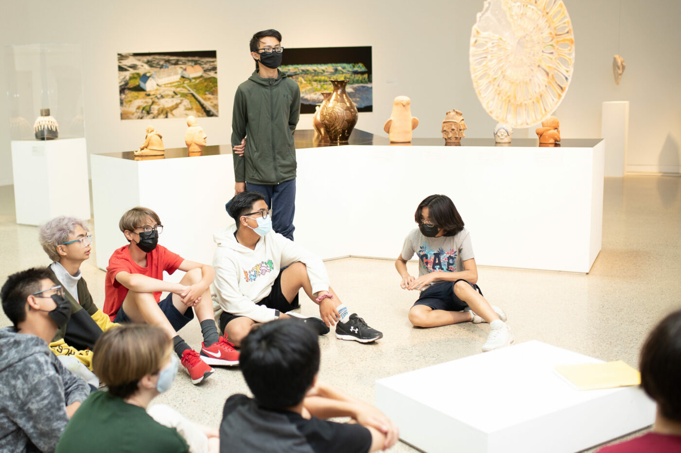 Young people sit on the floor of the gallery and listen to an educator speak.